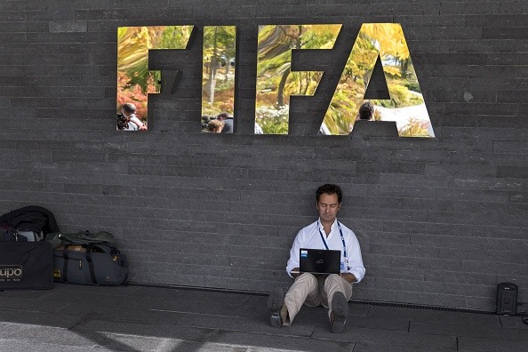 A journalist works on his laptop as he sits under the FIFA logo 